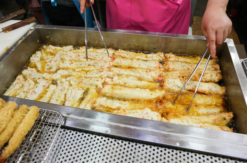 A vendor fries eomuk in a large pan of hot oil at a market stall.