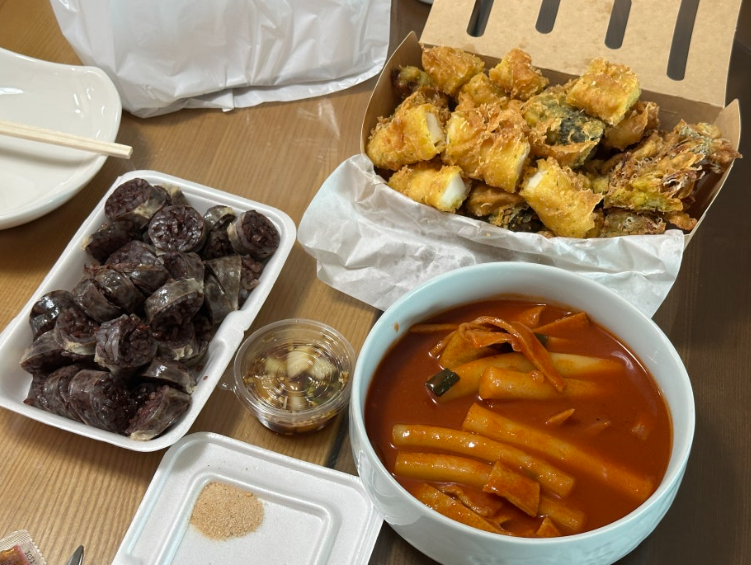 An assortment of golden twigim served with tteokbokki and sundae, with dipping sauce on the side.