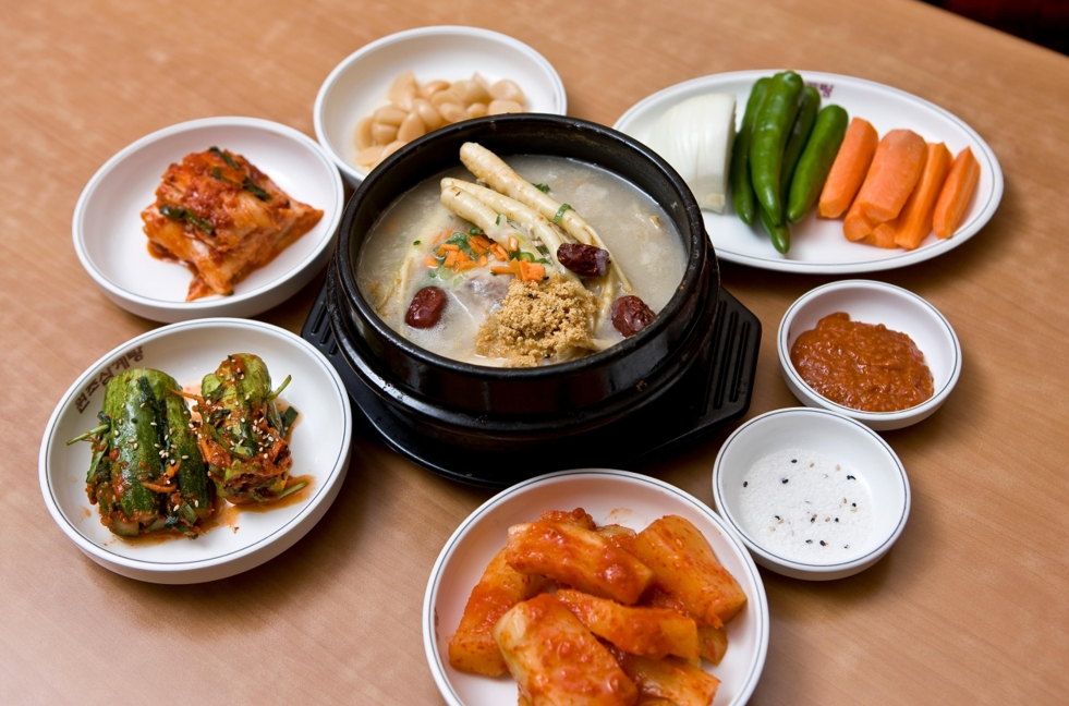 Samgyetang served in a ttukbaegi (뚝배기) with kimchi, kkakdugi (cubed radish kimchi), seasoned vegetables, and dipping sauces.
