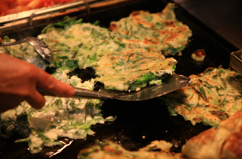 Freshly made pajeon is cooked on a large griddle until golden and crispy.
