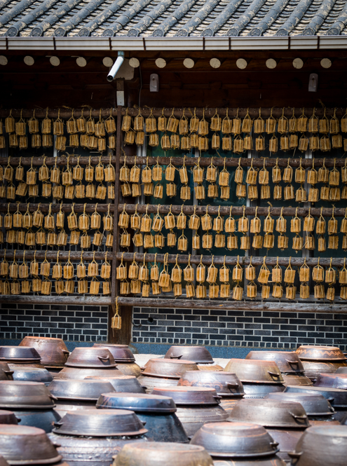 Rows of meju (메주) hang beneath the eaves, while onggi (옹기) jars sit in the foreground.
