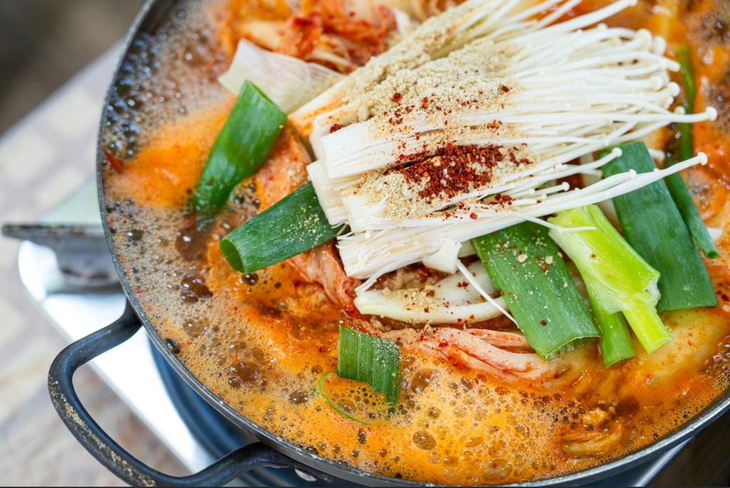 A bubbling pot of kimchi jjigae (김치찌개), made with well-fermented kimchi and topped with enoki mushrooms and green onions.
