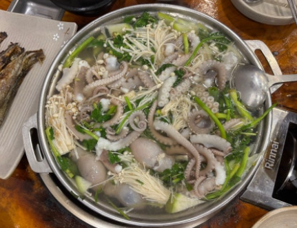 A shared pot of yeonpo-tang (연포탕), a mild Korean octopus soup with fresh octopus, enoki mushrooms, and greens in a clear broth. It is usually ordered for the table to share, rather than as an individual serving.