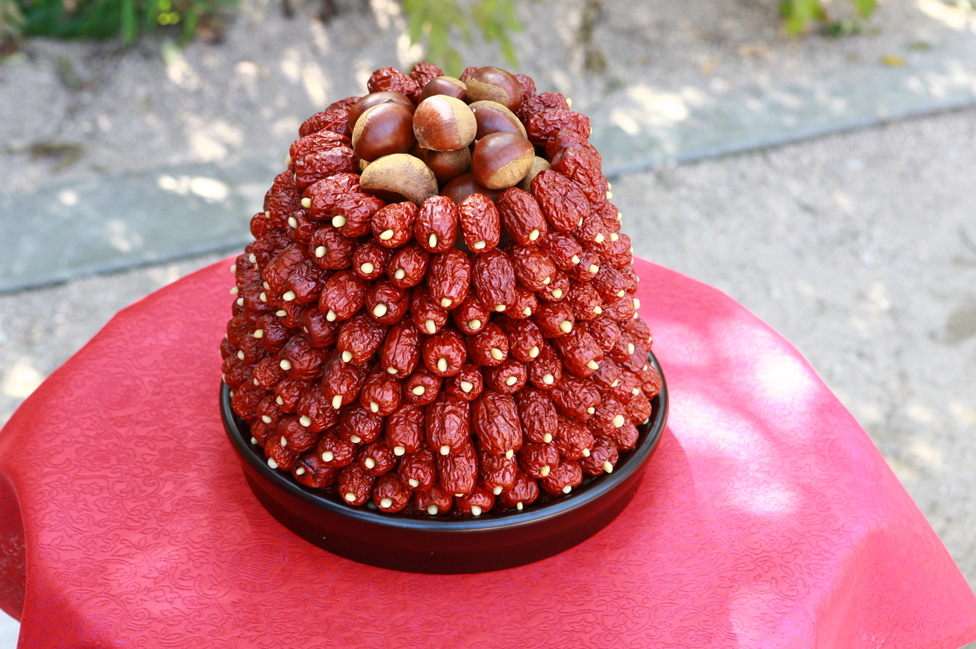 A decorative tower of dried jujubes topped with chestnuts is displayed on a red-covered table for a traditional Korean pyebaek wedding ceremony.