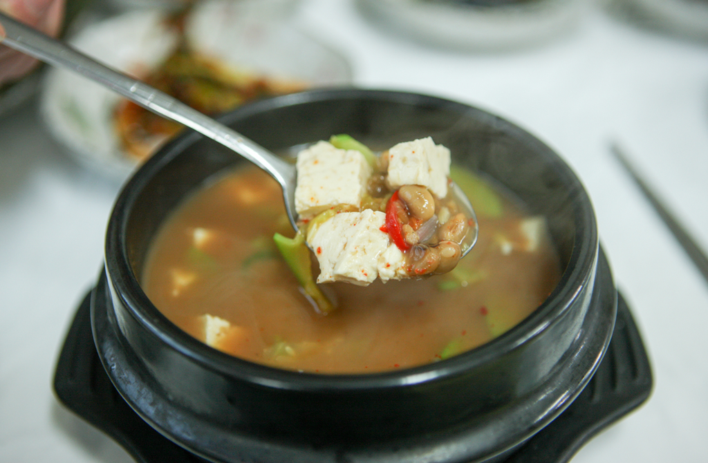 Korean Doenjang (된장): Fermented Soybean Paste A spoonful of doenjang jjigae (된장찌개), Korean soybean paste stew with tofu, zucchini, mushrooms, and red chili, served in a black ttukbaegi (뚝배기).