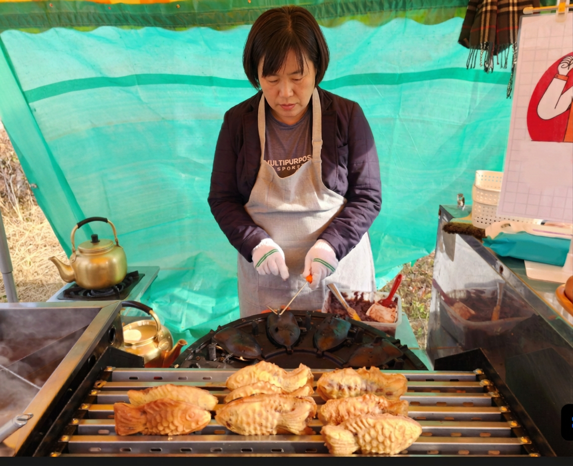 A vendor cooks bungeoppang at a street stall, with freshly baked pastries arranged on the counter in front.